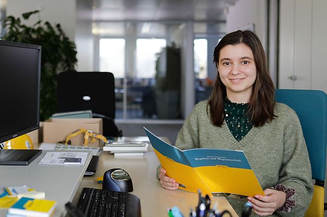 Unsere KV-Lernende studiert einen Prospekt an ihrem Arbeitsplatz im Büro