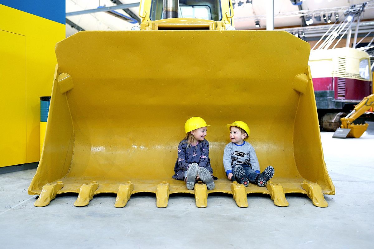 Zwei strahlende Kinder sitzten nebeneinander in einer Schaufel im EBIANUM Baggermuseum in Fisibach 