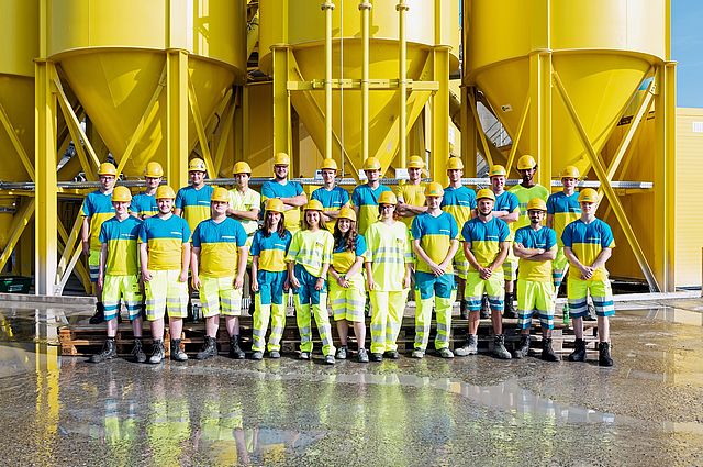 Unsere Lernenden werfen ihre Bauhelme vor den Silos in die Luft