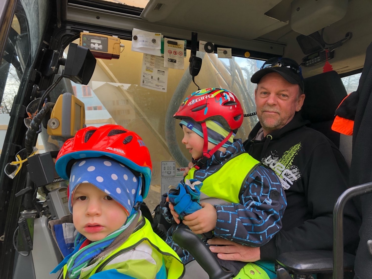 Dario und Yannick mit Baggerführer Erwin im Bagger auf der Baustelle in Kloten