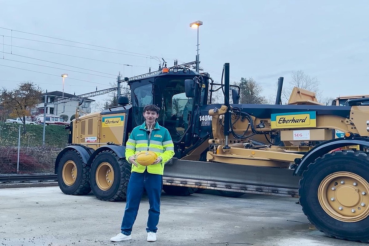 Ein Lernender steht vor einer Baumaschine.